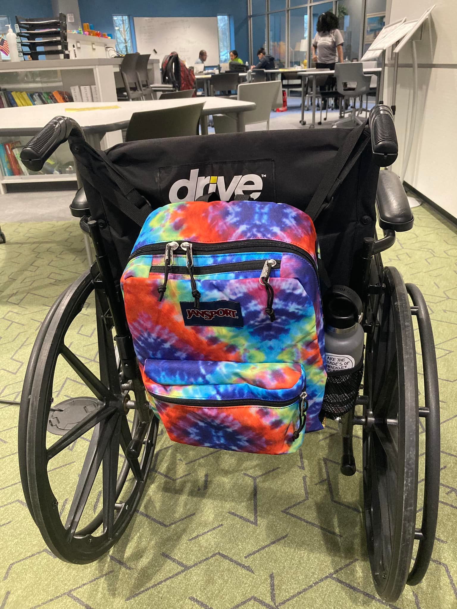Please enjoy this picture of my new bag hanging on the back of my wheelchair. It's a Jansport adaptive collection backpack in tie-dye. It has loops to hang on the handles of my wheelchair and one that could hang it on the neck rest of certain electric wheelchairs. Also it has organizer pockets. My work stuff is so much more organized than in the tote bag I was hauling it around in.

I have heard a lot of people say that their chairs are like an extension of their body, and I got it I intellectually, but after two months of using mine five days a week I'm really attached to it.