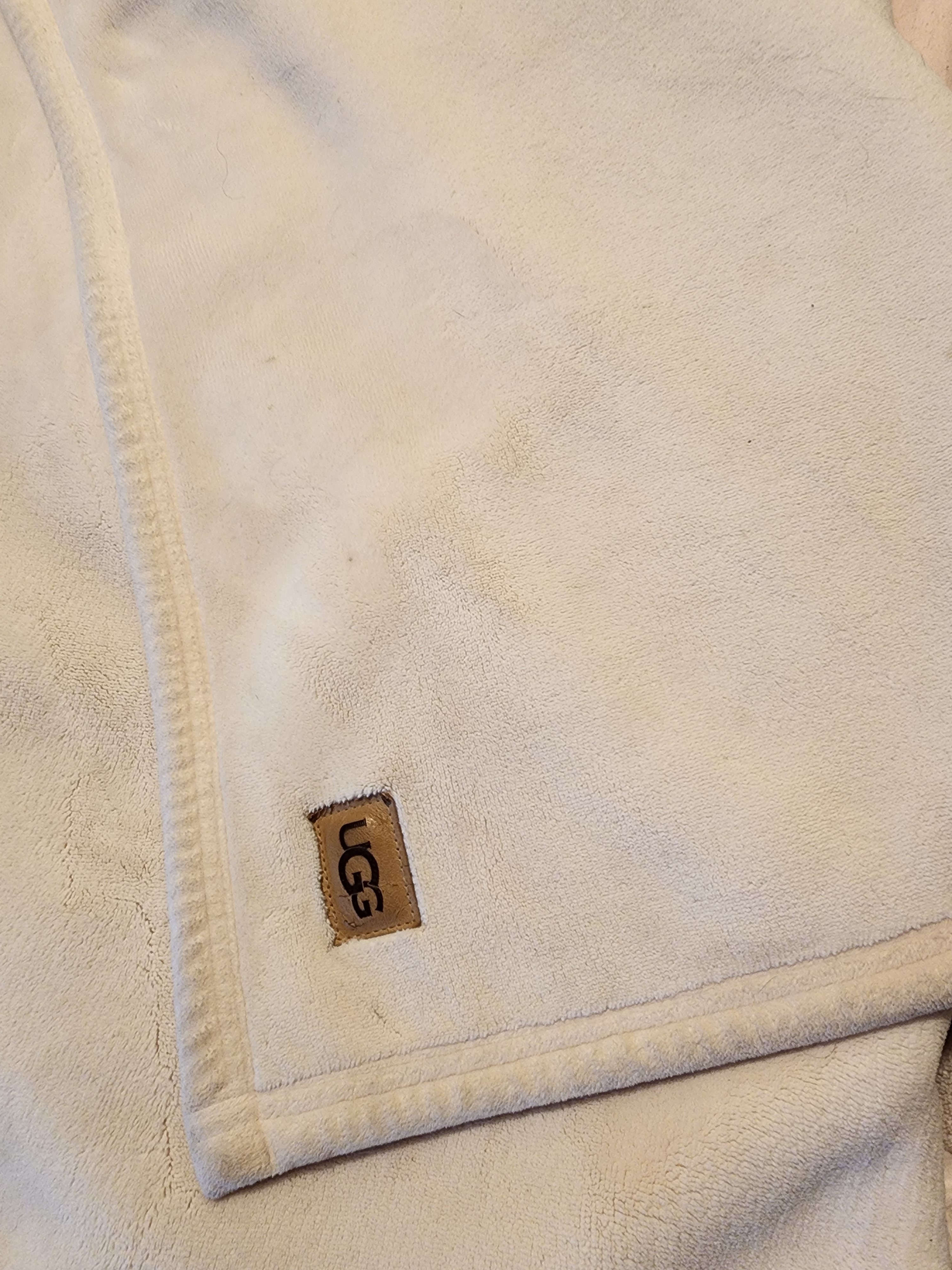 Plain white, plush blanket with faux leather UGG logo visible