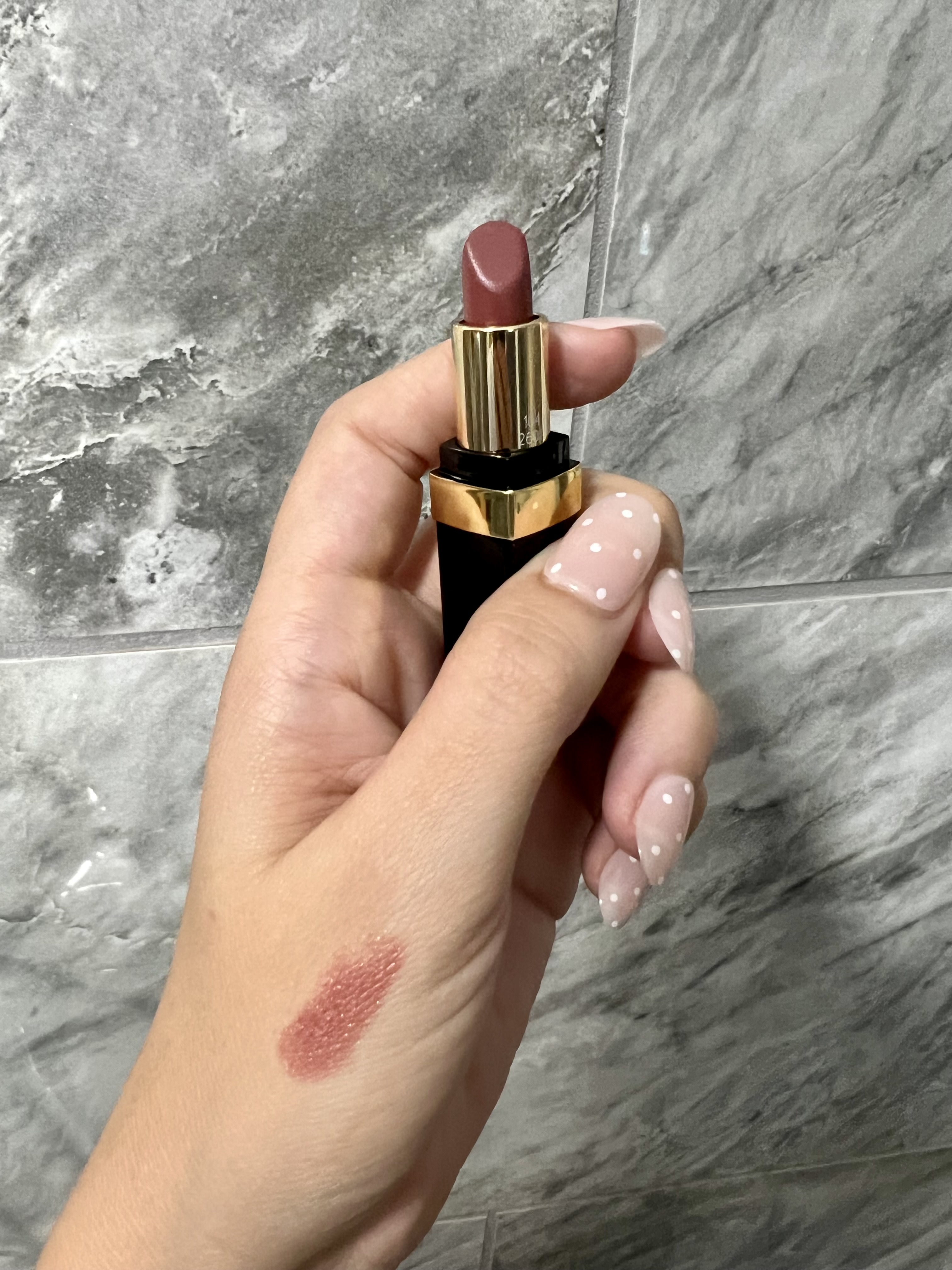 Hand holding up Chanel lipstick with swatch on hand