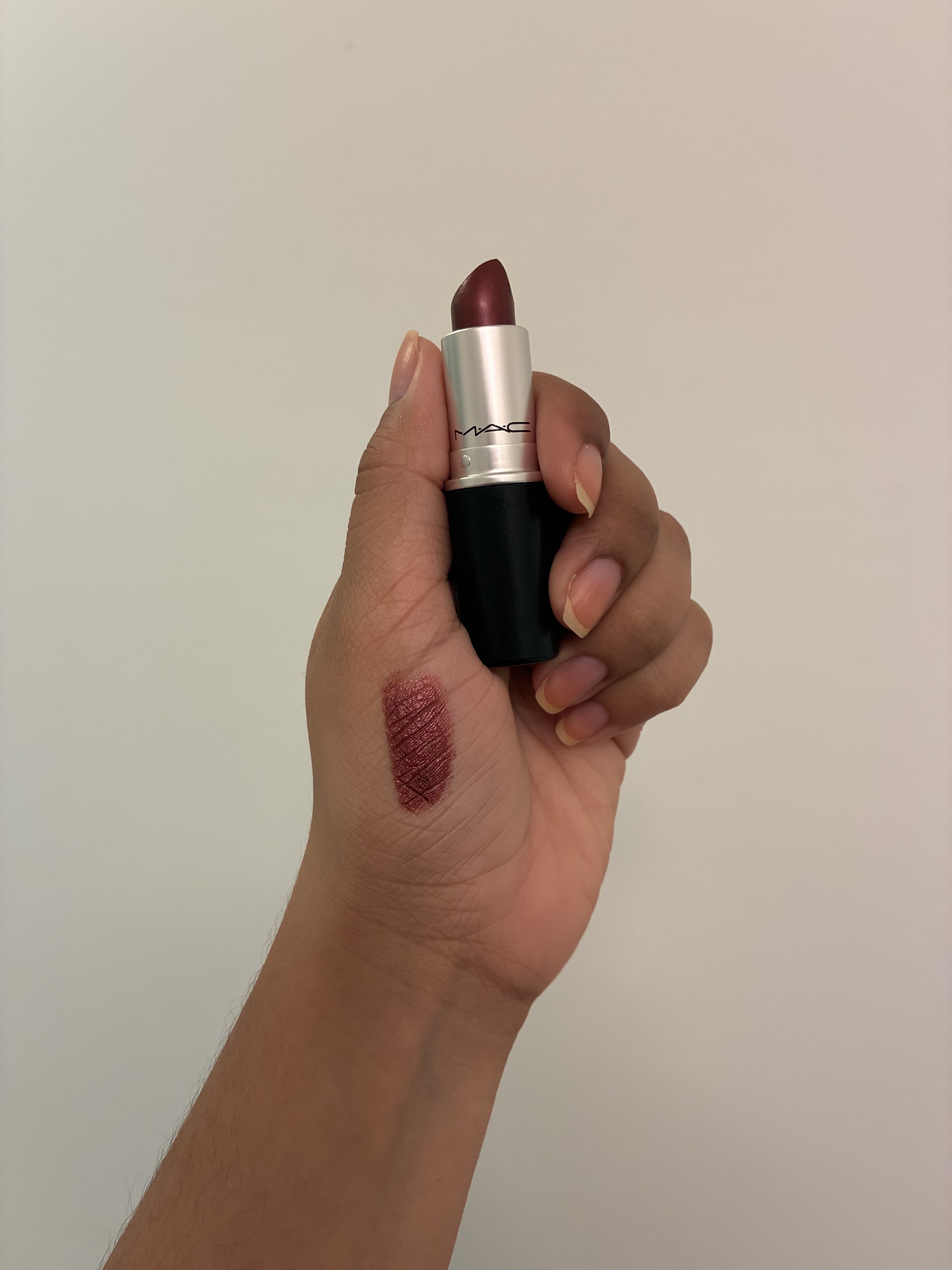 Hand holding open lipstick with swatch on palm.
