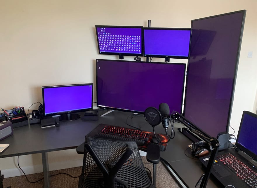 Home office - one 43 inch monitor horizontal as main, one 43 inch monitor in portrait at the side, two 21 inch monitors above main, 1 21 inch monitor to the left and a laptop to the right of everything. Microphone on moveable arm