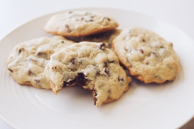 5 home-baked chocolate chip cookies piled on a plate. One has a bite out of it.