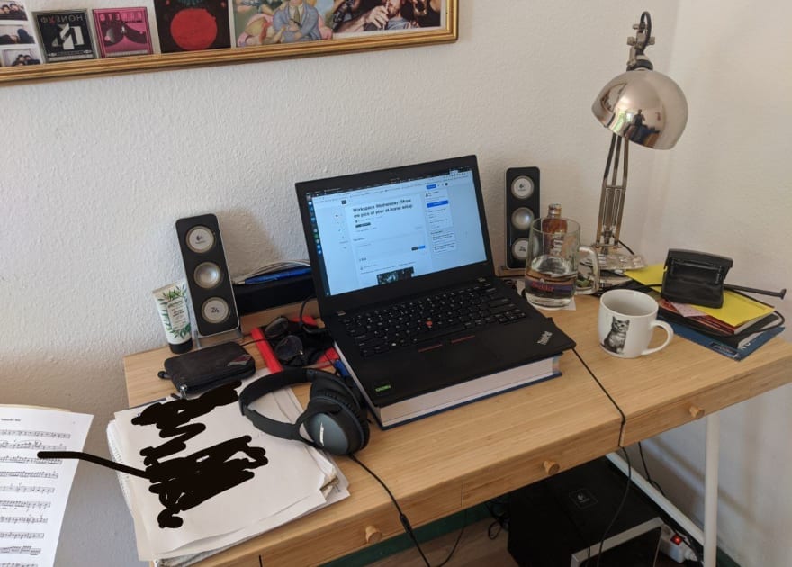 Small messy desk with a laptop, some speakers, a coffee cup with a cute cat and stacks of random paper