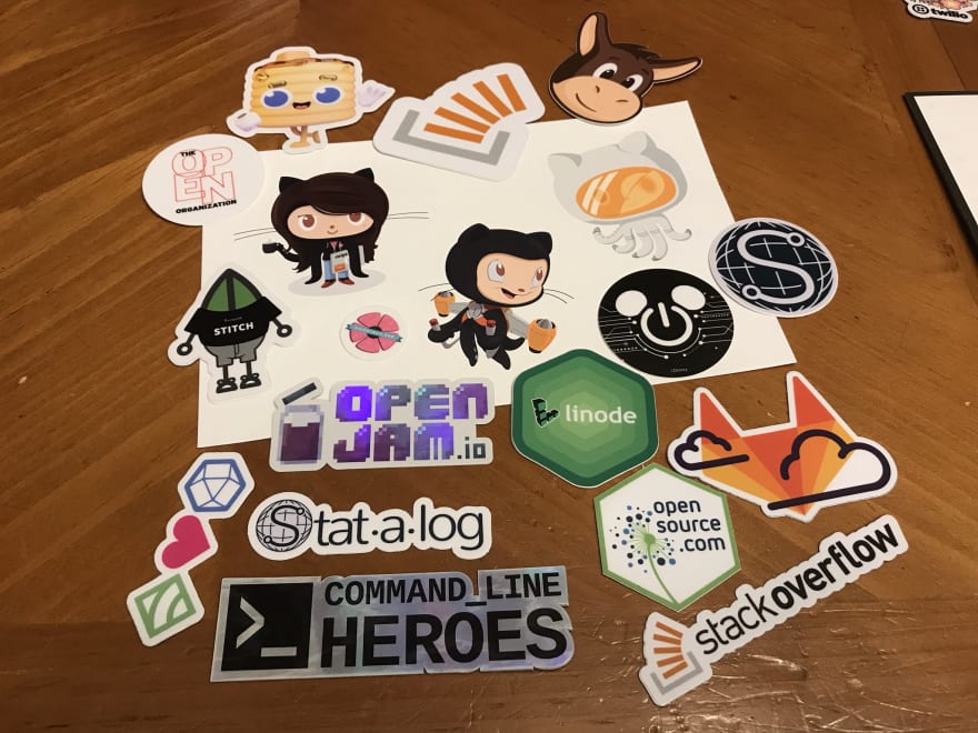 bunches of stickers showing just a name, mascot, or logo. Credit for these stickers (Github, OpenJam, Stack overflow, opensource.com, GitLab, MongoDB, Statalog.org, Disney Tech, Stickermule, YourStacks, The OPEN organization, Linode, ChickTech)