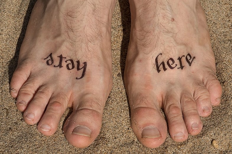 Feet tattooed with Stay Here