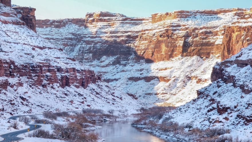 Red desert cliffs coated in snow tower above the Colorado River outside of Moab, Utah in wintertime.
