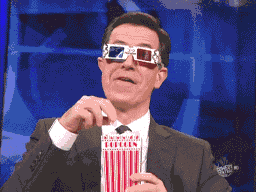 Stephen Colbert eating popcorn with 3D glasses and smirking