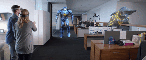 A gif of two people wearing a HoloLens. The people are looking at a holographic robot walking in their direction. A holographic alien creature is standing to the right of the people..