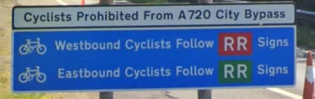 A road sign telling cyclists to follow markings to go East or West. The marking is the same except for its background colour being red or green
