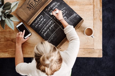 Looking down on a table with a chalkboard on which a woman is writing a meal plan