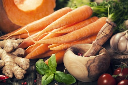 A table covered with carrots, tomatoes, and various herbs and root vegetables.