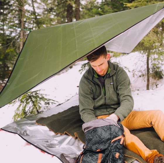 A photo of a man sitting on top of an Arcturus blanket while underneath another blanket