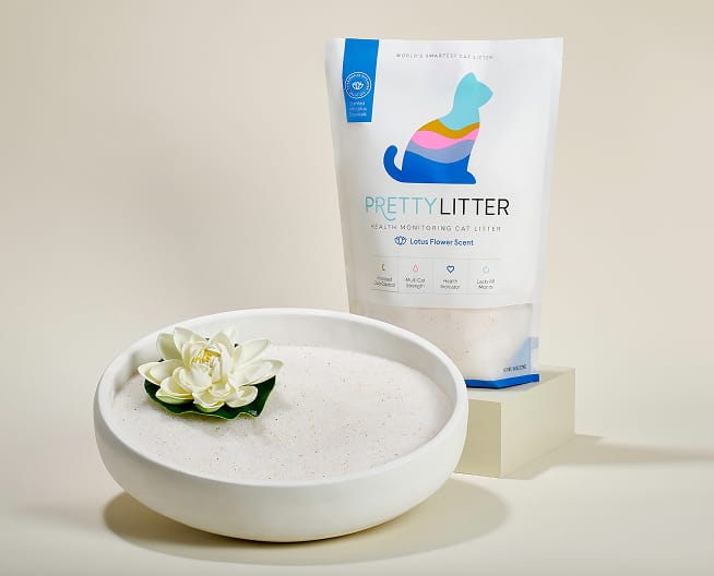 A package of PrettyLitter with lotus flower scent placed on a marble platform with vases and flowers in the background