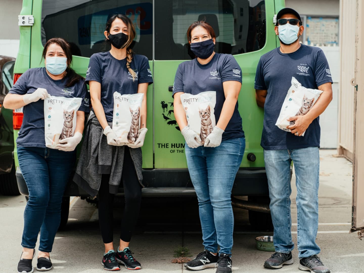Four people in masks holding PrettyLitter bags in front of a green van