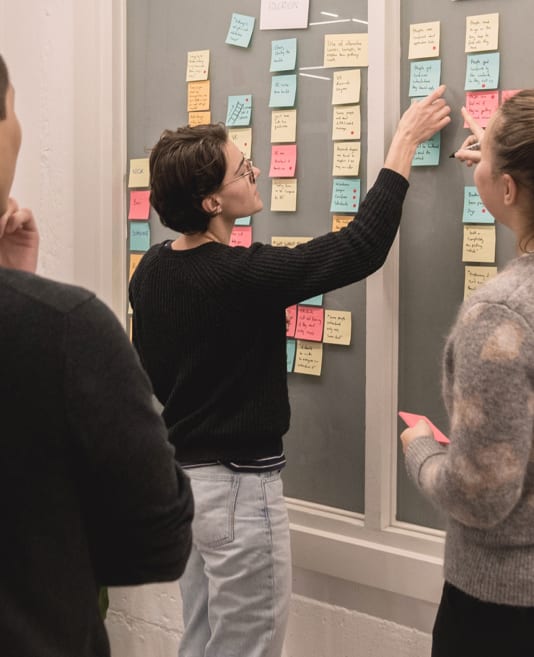 Three people looking and pointing to a wall with post it notes