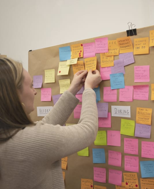 Person reaching for a sticky note on a board