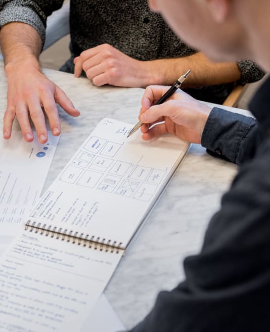 Person's arm holding a pen above a notepad