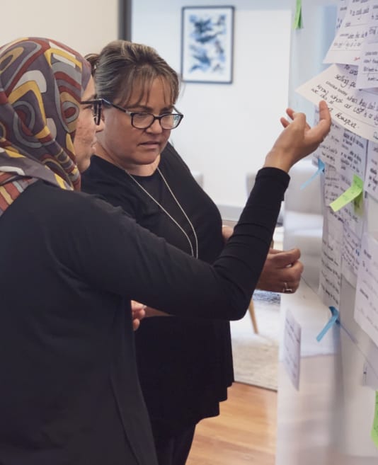 Two people discussing near a whiteboard of sticky notes