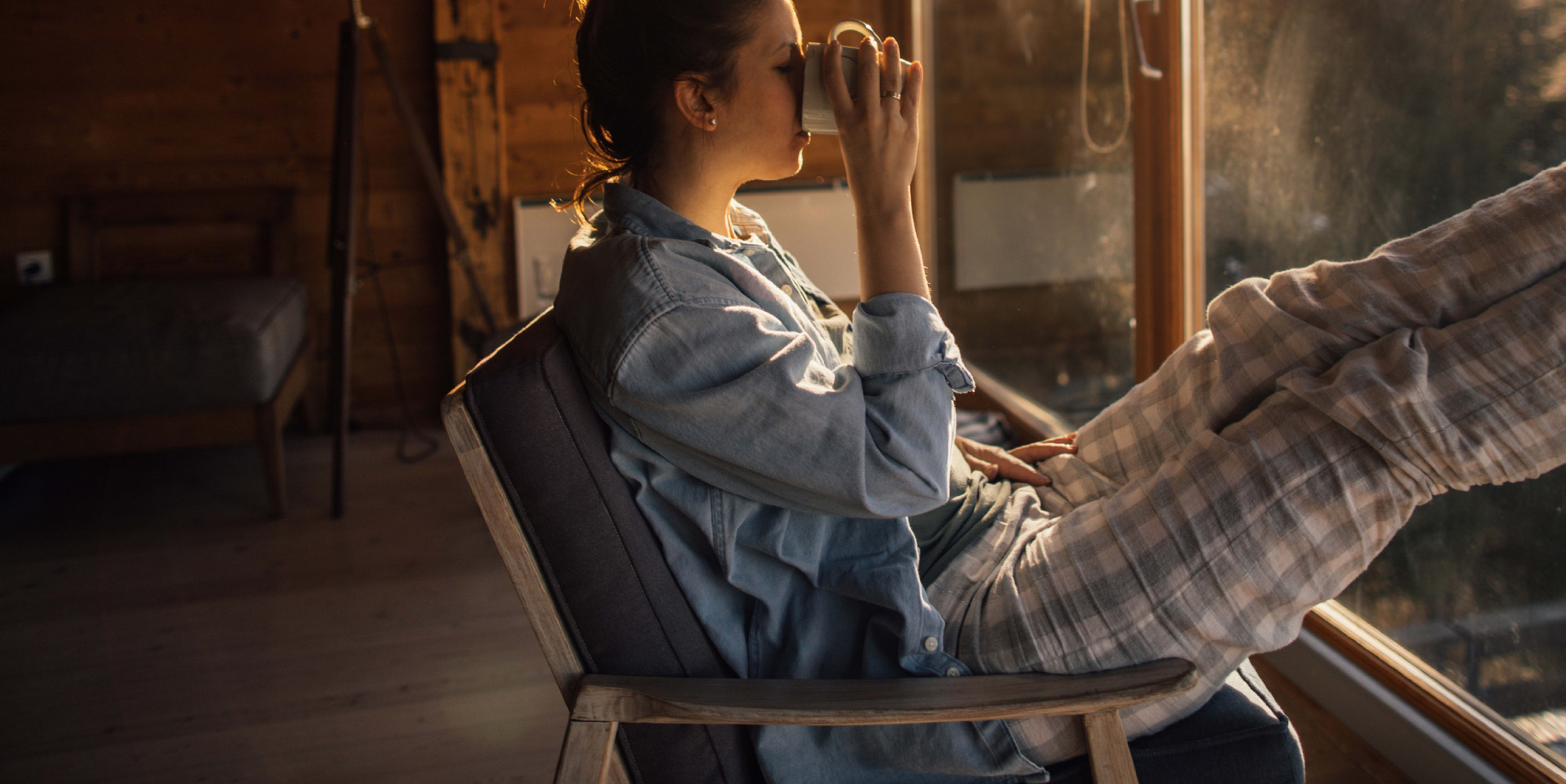 Person sitting on a chair near a window with a beverage