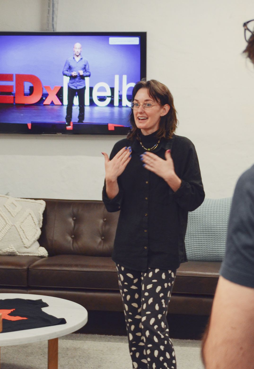 Woman speaking to a small group, in front of a tv with TED-X on the screen