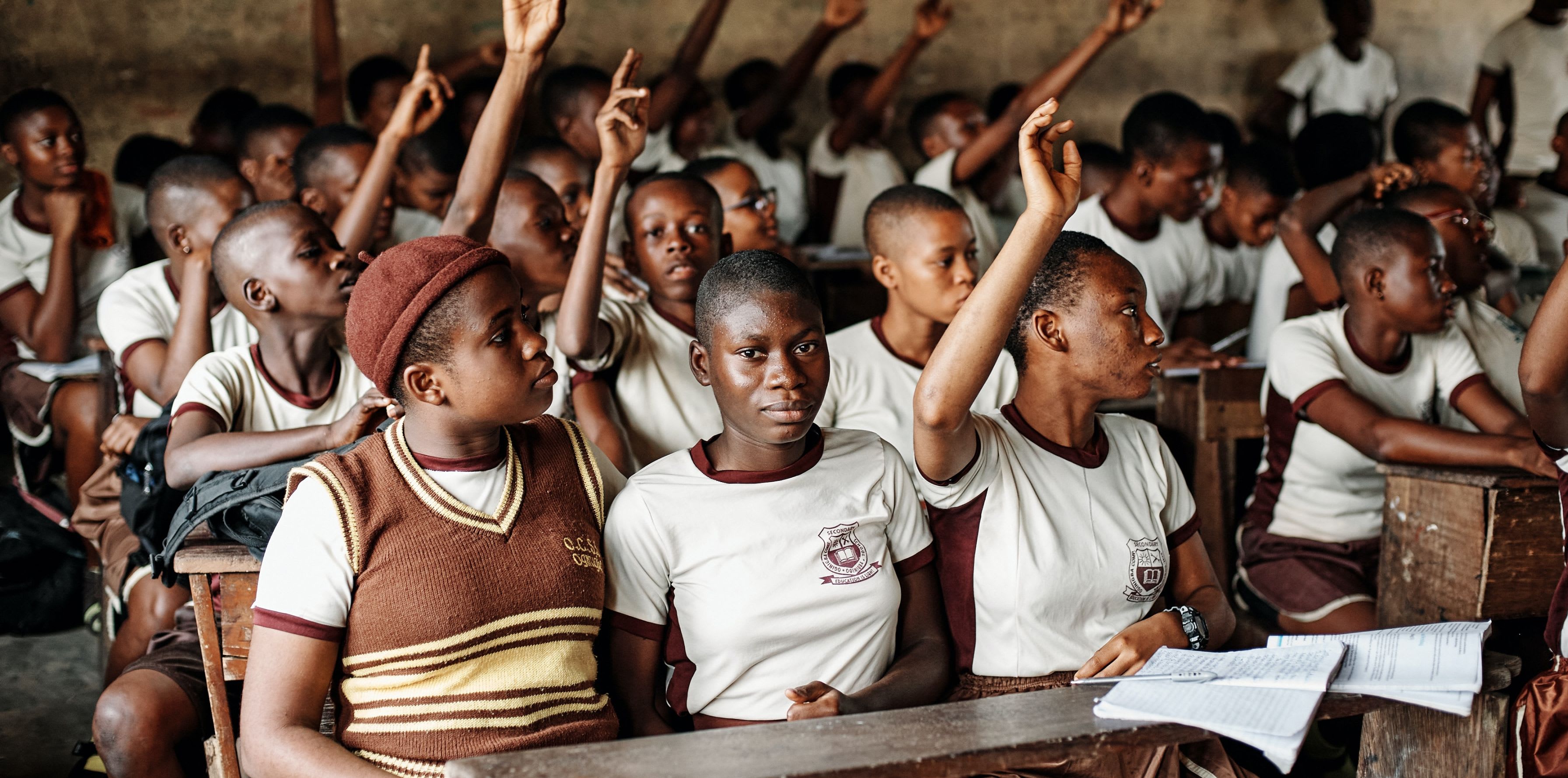 A classroom of Nigerian teenagers raise their hands to answer a question
