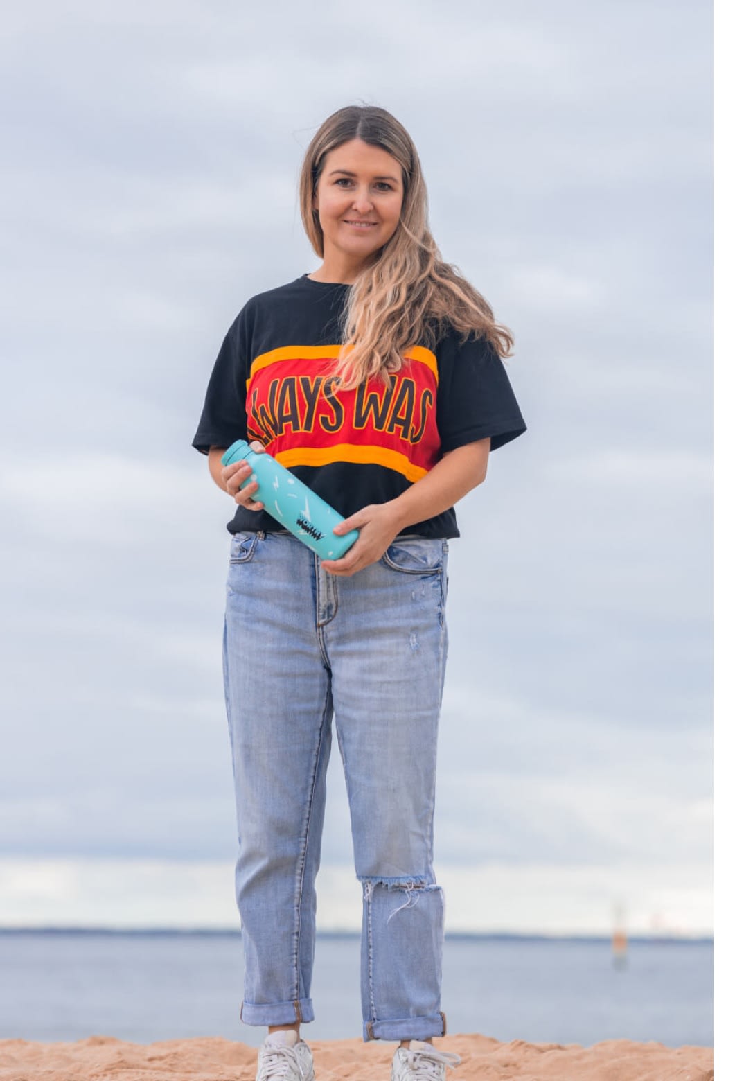 A woman standing on the beach holding a water bottle