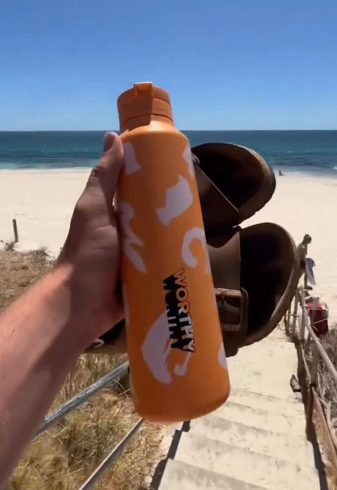 A person holding a bottle and sandals at the beach 