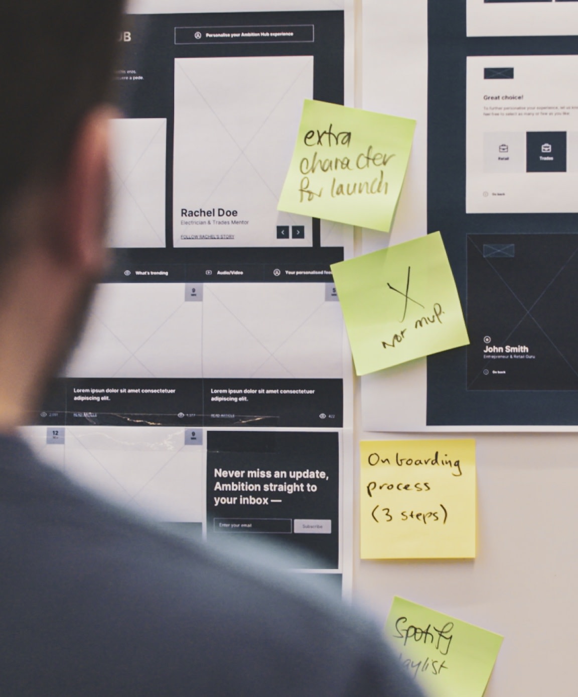 A board of sticky notes and wireframes as the focus with a person looking on in the background