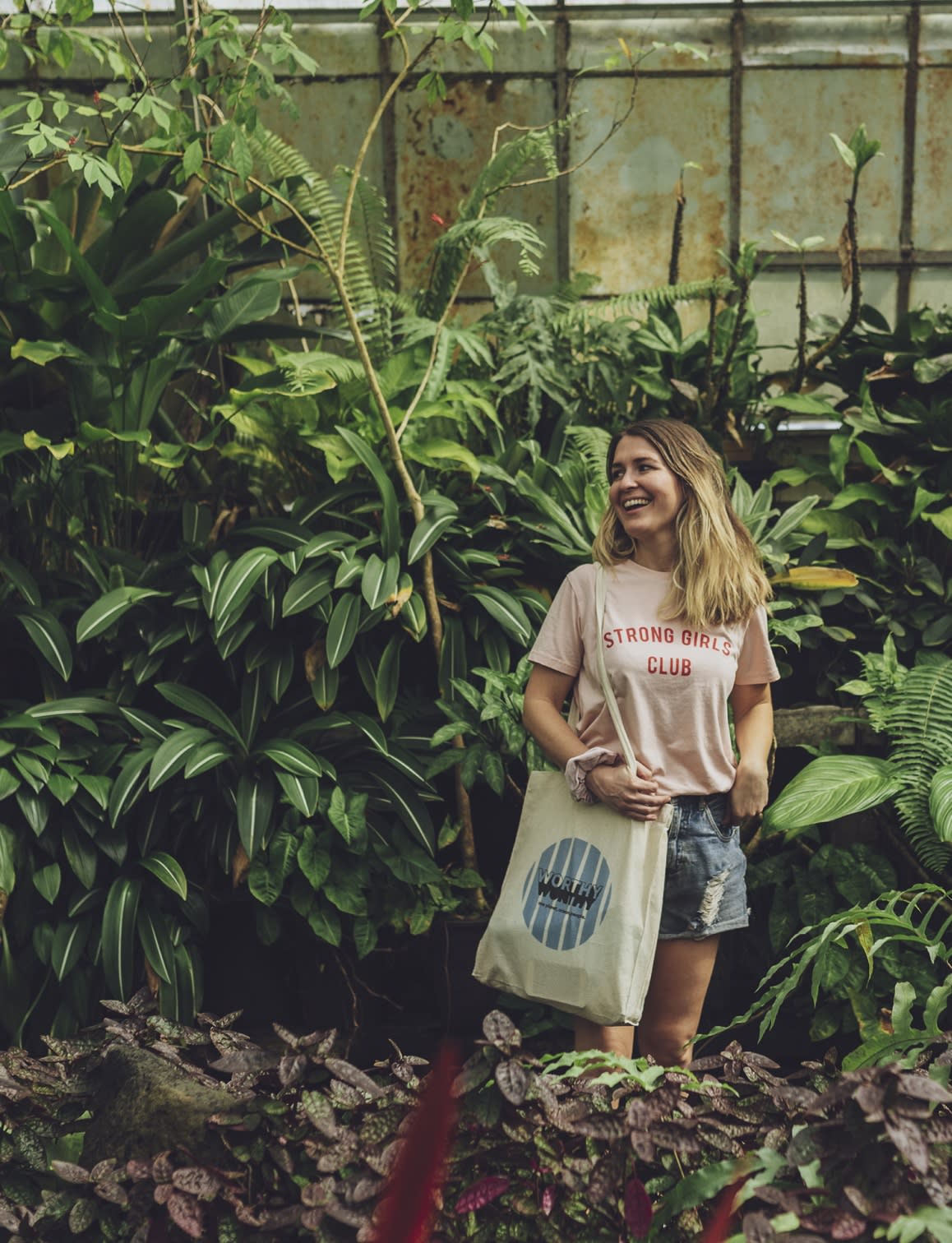 Person standing with a tote bag against a background of green plants