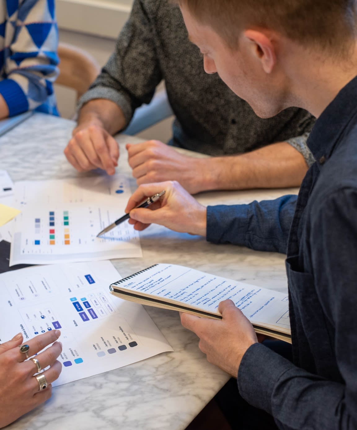 Person holding a notebook in one hand and a pen in the other pointing to wireframes
