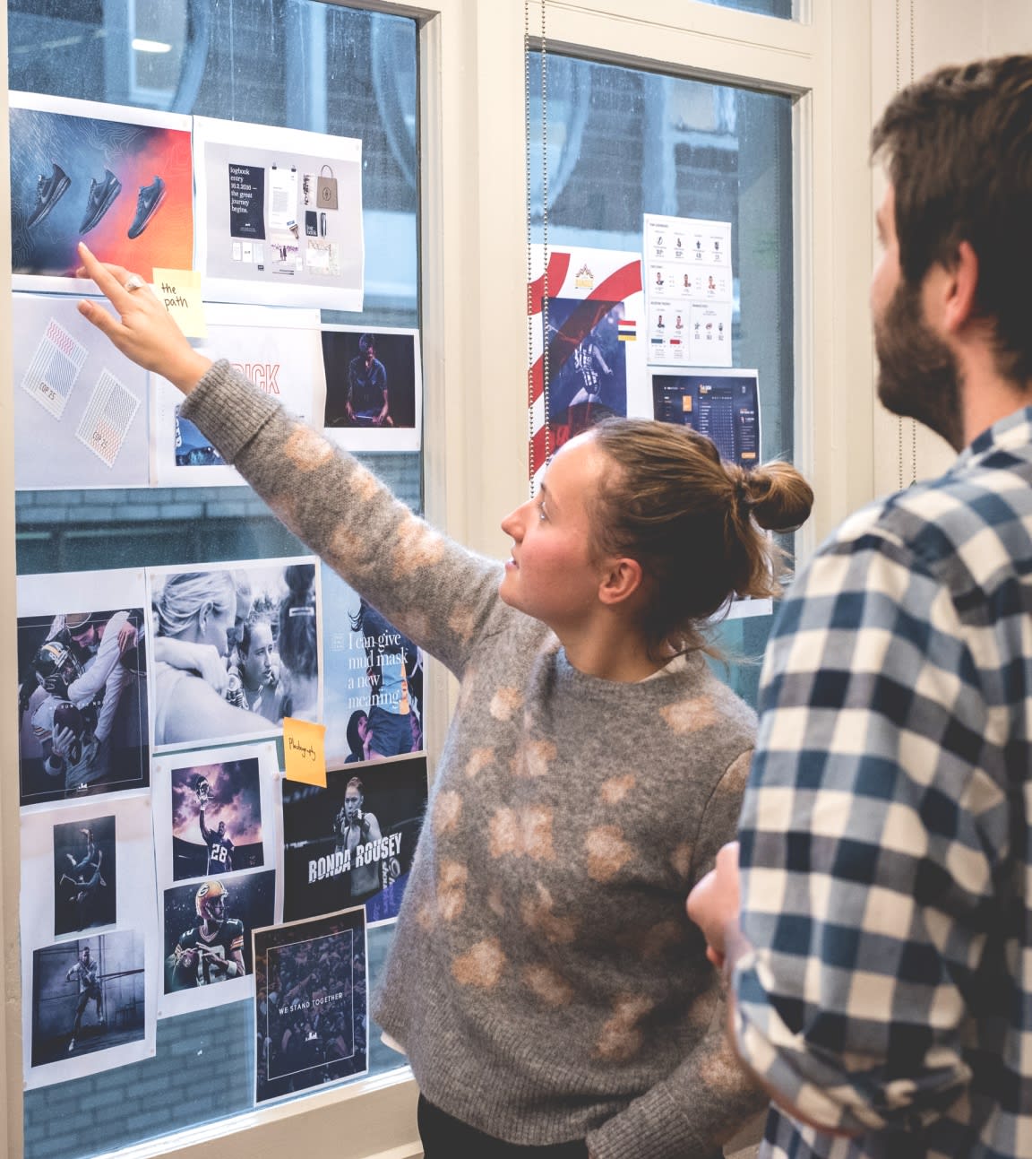 On person pointing at notes stuck on a window with another person looking on