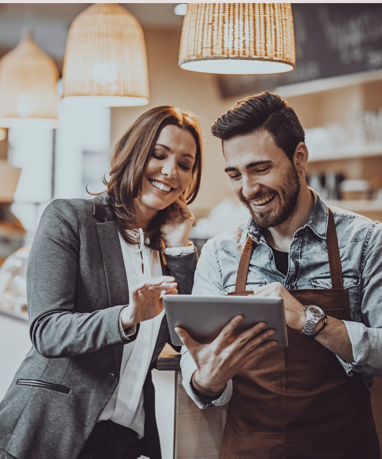 A business woman and a cafe shop owner smiling while looking at a tablet device