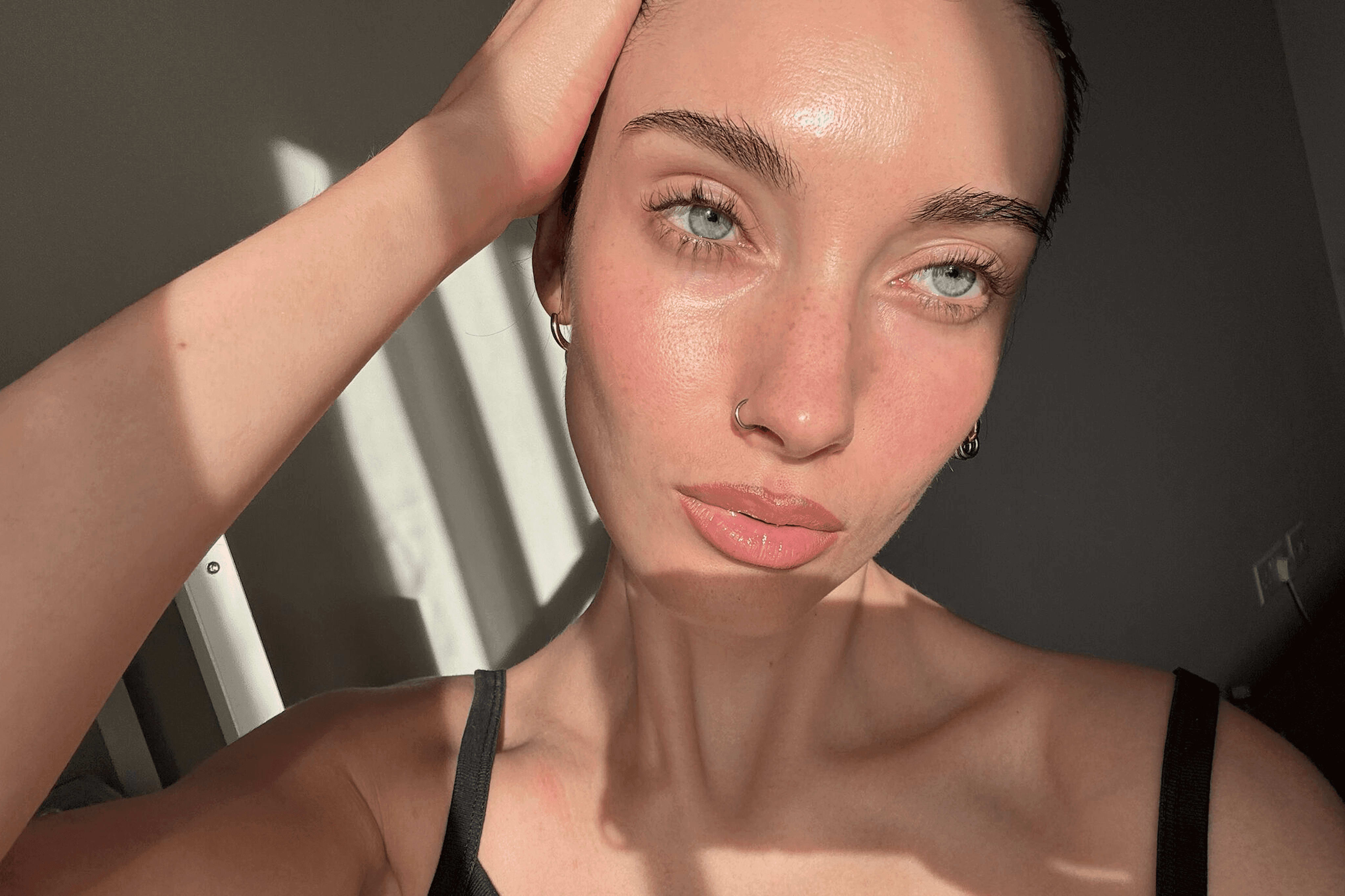 Close-up of a woman with dewy, glowing skin posing in natural light, highlighting hydrated texture and a minimal skincare look.