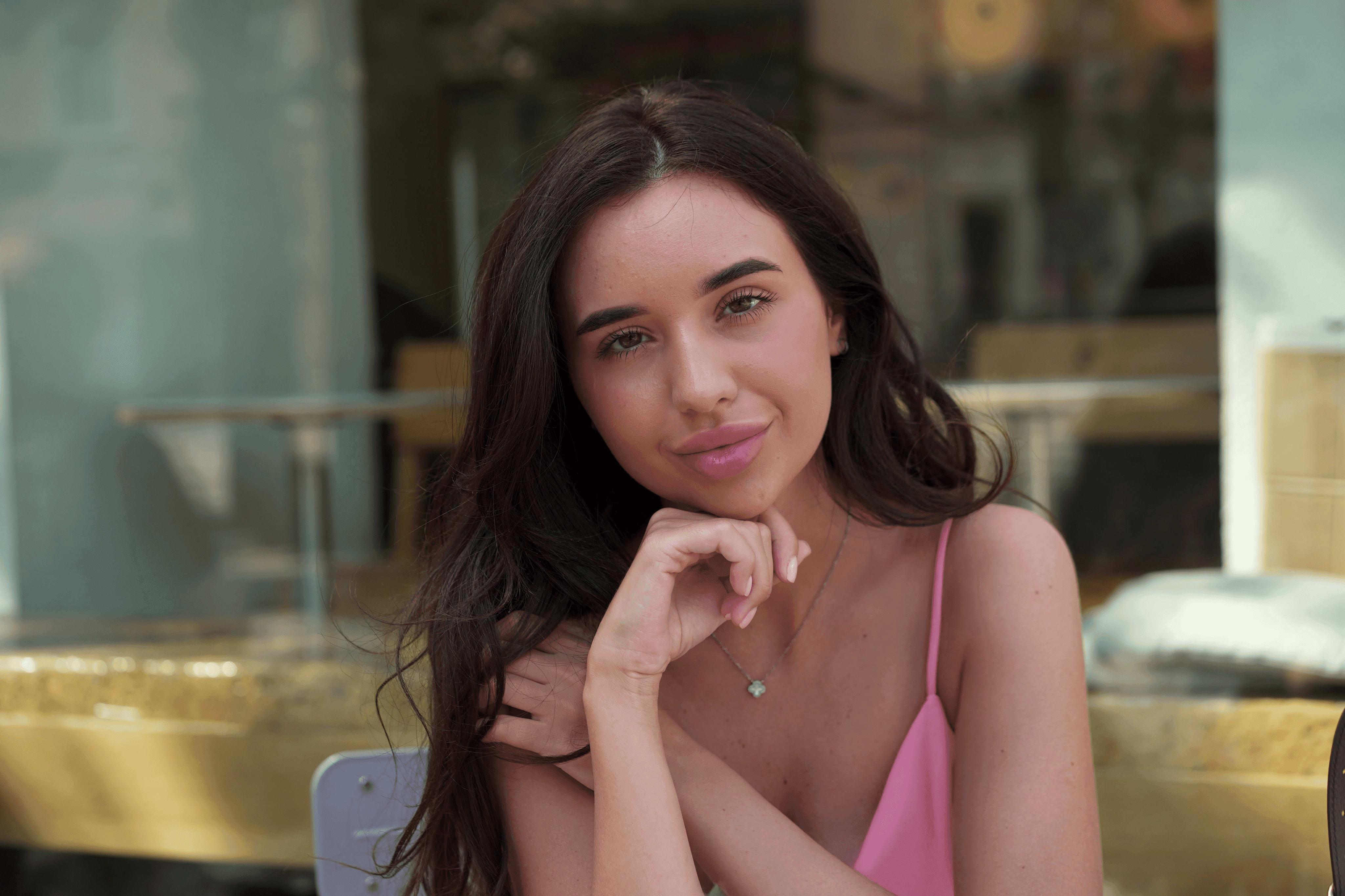 Portrait of a woman sitting at a café table, resting her chin on her hand, with a soft natural makeup look and a relaxed, confident expression.