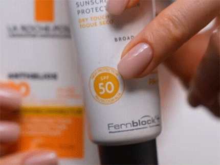 Close-up of a finger pointing to the SPF 50 label on a Heliocare sunscreen bottle.