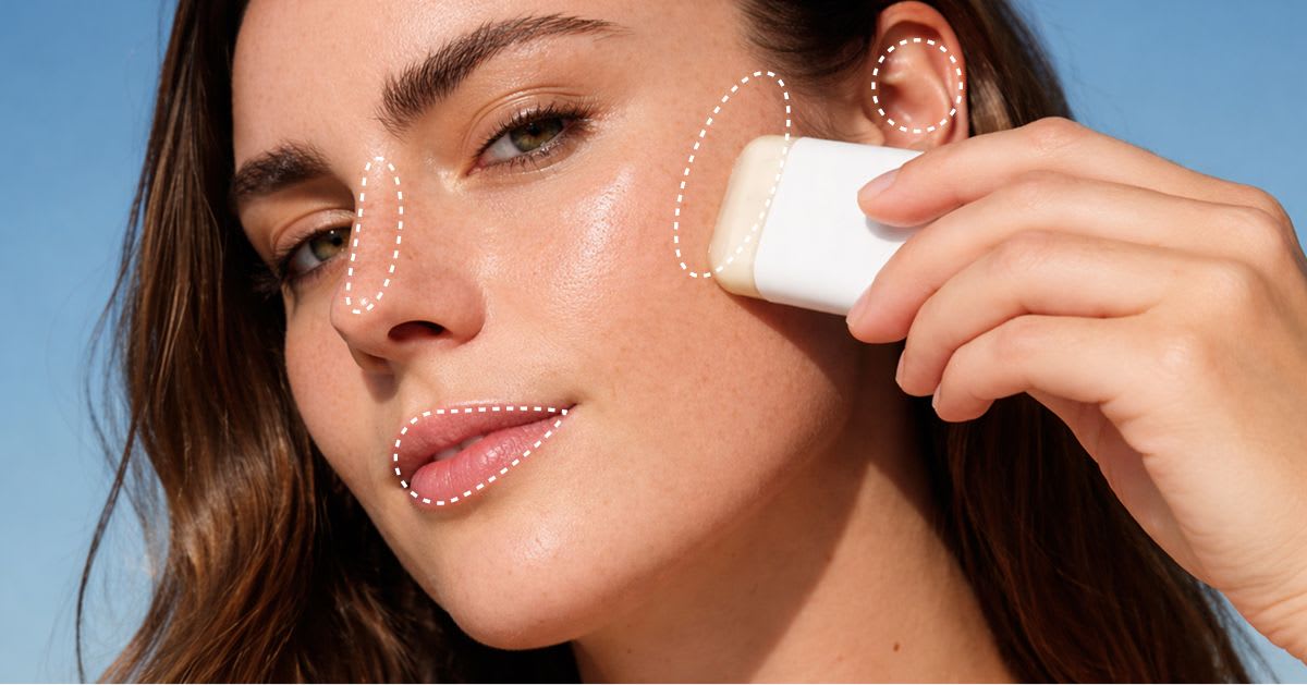 Woman applying a sunscreen stick to her face with dotted outlines marking the high-exposure areas: nose, cheekbones, ears, and lips.