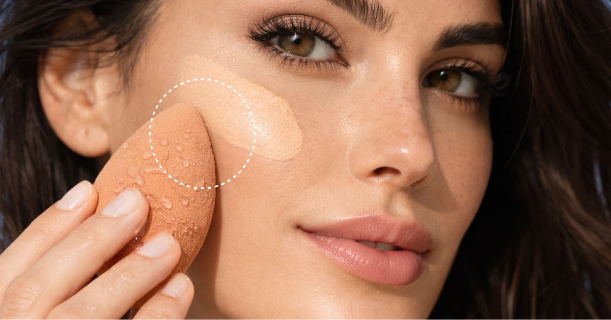 Woman pressing foundation onto her cheek with a damp beauty sponge to avoid disturbing the sunscreen layer underneath.