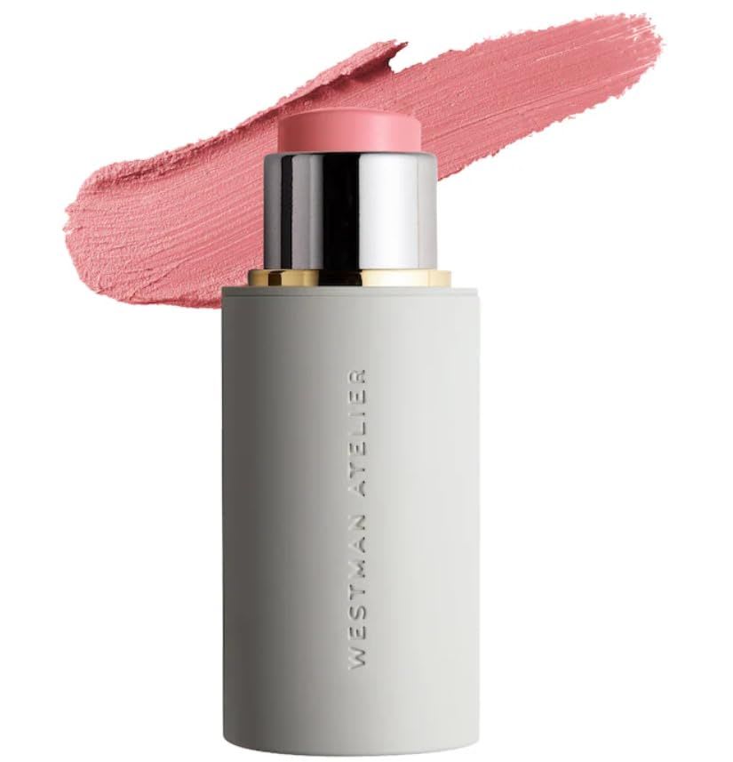 Westman Atelier Baby Cheeks Blush Stick in a soft pink shade, shown in a sleek light-gray cylindrical tube with a metallic silver and gold accent, with a matching pink blush swatch textured behind the product on a clean white background.