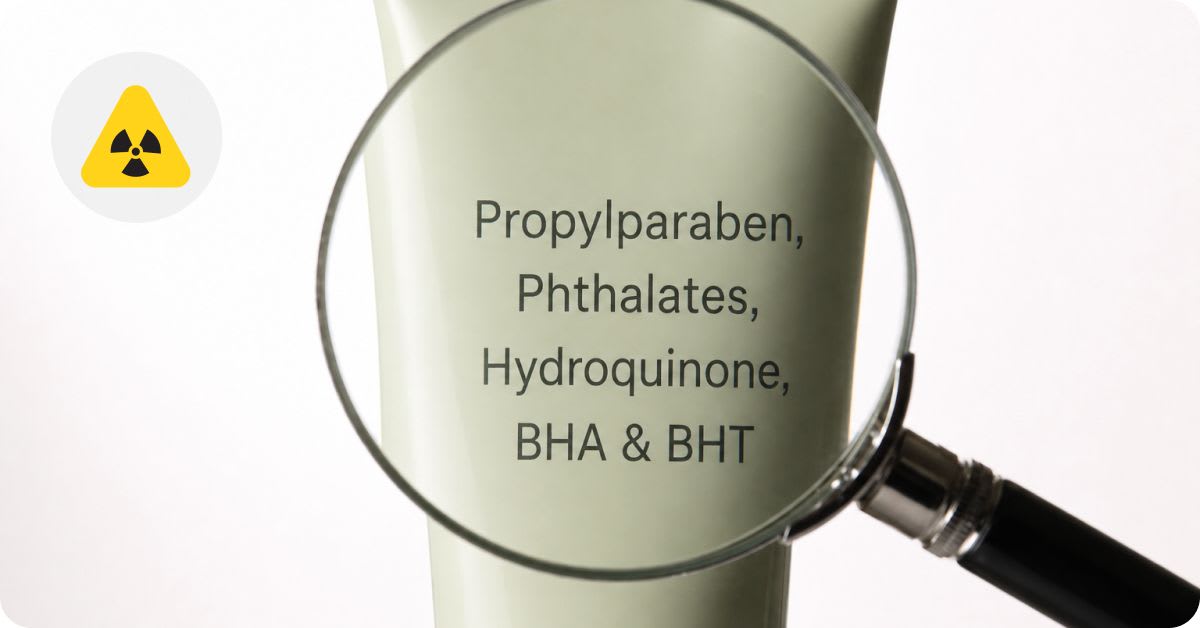 Magnifying glass held over a cosmetic tube revealing a list of harmful ingredients — Propylparaben, Phthalates, Hydroquinone, BHA & BHT — with a yellow hazard symbol in the corner, highlighting toxic chemicals to look out for in skincare products.