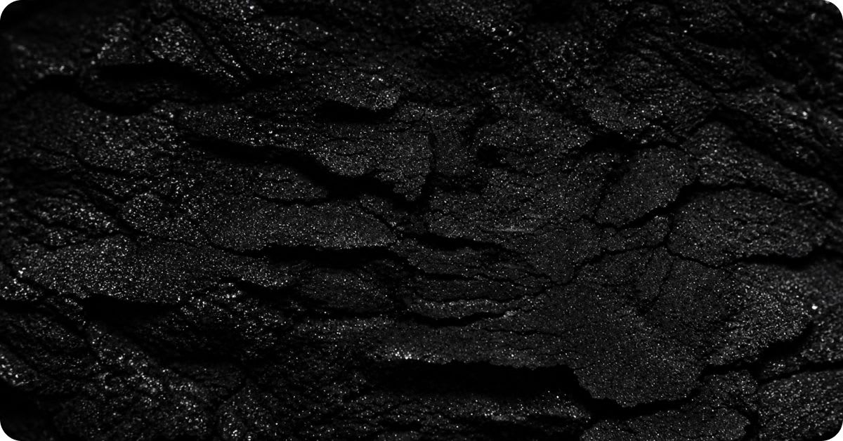 Close-up texture of thick, rough black tar with a glossy crusted surface, representing coal tar — a petroleum-derived ingredient linked to potential health risks in cosmetic products.