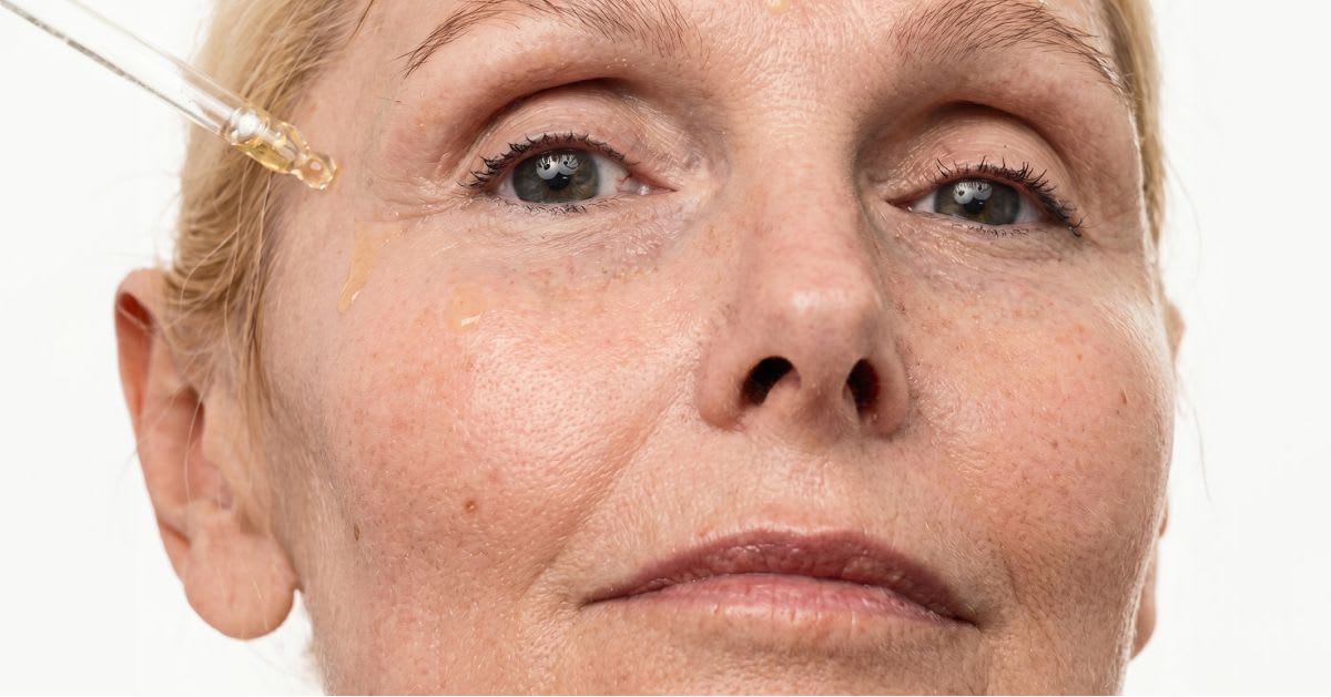 Close-up of mature woman applying eye serum with dropper to fine lines around the eye