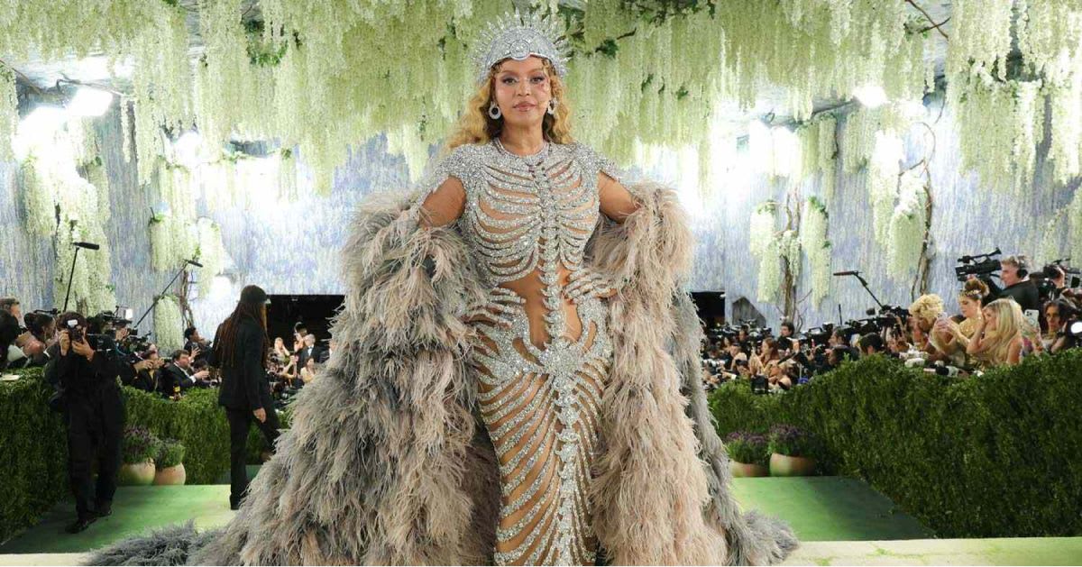 Beyoncé — Beyoncé at the 2026 Met Gala in a sheer crystal-embellished gown with a ribcage-structured bodice, voluminous feathered cape, and a jeweled crown headpiece