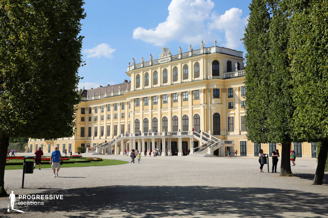 This majestic Baroque palace features an ornate yellow façade adorned with classical statues, arched windows, and decorative balustrades. A grand double staircase leads to the upper terrace, enhancing the palace’s sense of scale and elegance. Symmetrically placed manicured gardens and gravel pathways frame the scene, while towering trees provide a natural border, drawing attention to the architectural splendor. The palace’s harmonious design and historical grandeur make it an ideal filming location for period dramas, royal narratives, or sophisticated historical reconstructions, offering an opulent backdrop for scenes set in aristocratic or imperial settings.