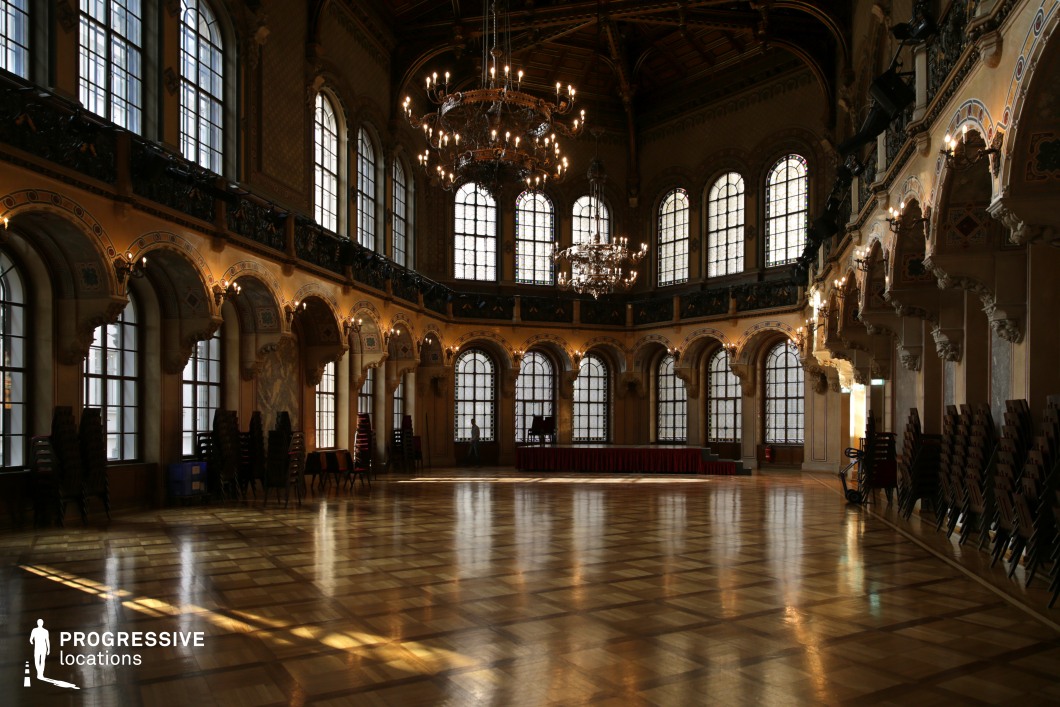 This opulent ballroom features soaring arched windows, intricate wall detailing, and a polished parquet floor that reflects the glow of grand chandeliers. The rich architectural elements, including carved archways, decorative moldings, and an upper-level balcony, contribute to the hall’s regal atmosphere. The dim, atmospheric lighting enhances the contrast between the warm golden tones of the walls and the dark wooden ceiling, creating an intimate yet grand setting. This location is ideal for period dramas, historical epics, or aristocratic events, providing an elegant backdrop for ballroom scenes, high-society gatherings, or dramatic confrontations.