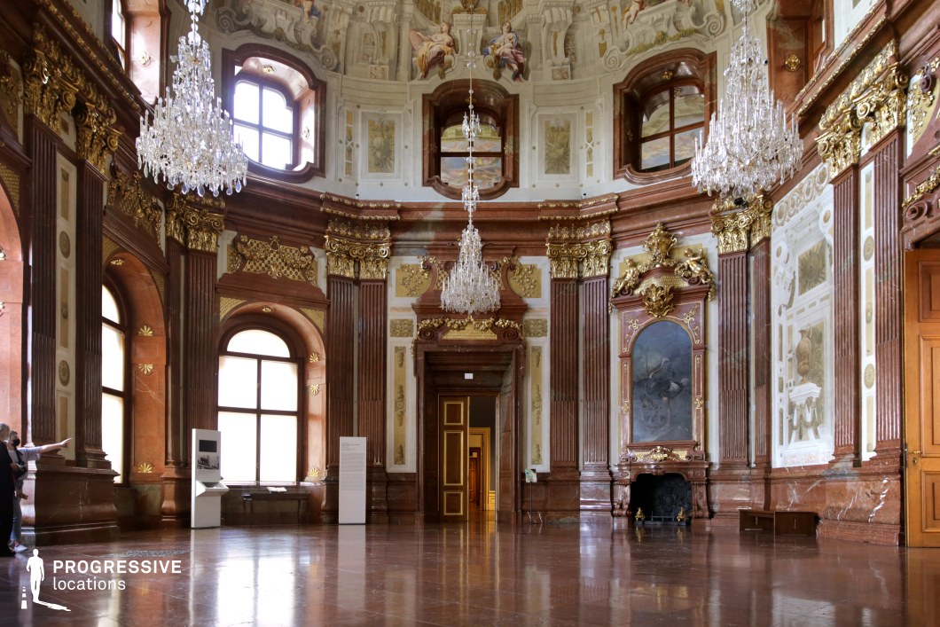 This grand Baroque-style hall exudes luxury with its towering marble columns, gilded ornamentation, and intricate frescoes adorning the high, vaulted ceiling. Large arched windows allow soft, natural light to illuminate the polished red marble floors, highlighting the rich textures and craftsmanship. Sparkling crystal chandeliers hang majestically, reinforcing the room’s regal atmosphere. Decorative wall panels, intricate gold moldings, and classical paintings contribute to the historical elegance. This location is ideal for period dramas, aristocratic settings, and lavish historical productions, providing a visually stunning and immersive backdrop for grand, refined storytelling.