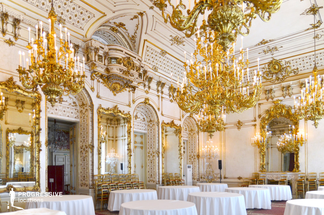 This opulent ballroom exudes grandeur with its intricate gilded moldings, ornate wall panels, and towering mirrors that amplify the room’s spaciousness. The ceiling is adorned with elaborate gold embellishments, while multiple grand chandeliers with cascading candle-like lights enhance the regal atmosphere. The symmetrical design, arched doorways, and finely detailed wall carvings reflect the extravagance of baroque and rococo styles. The space is ideal for filming historical dramas, royal events, and aristocratic gatherings, providing an authentic backdrop for ballroom sequences, high-society affairs, or period-era intrigue. The reflective surfaces and golden hues offer excellent lighting opportunities, making it a visually captivating setting.