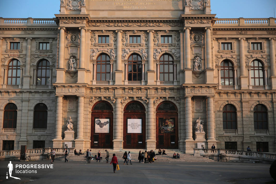 This imposing neoclassical building features an elaborately detailed stone facade with Corinthian columns, arched windows, and intricate sculptural reliefs. The grand entrance, marked by massive wooden doors framed by statues and decorative elements, exudes a sense of prestige and historical importance. The symmetrical design and balanced proportions give the structure a formal and authoritative presence, while the open plaza in front provides a spacious foreground for cinematic compositions. This location is ideal for historical films, intellectual dramas, or period pieces requiring a setting of cultural significance, elegance, and institutional power.
