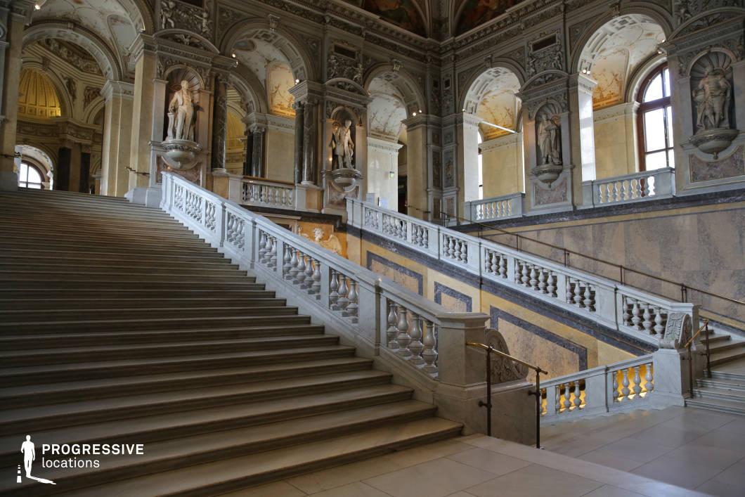 This monumental staircase, made of finely carved marble, ascends through a grand hall adorned with classical architectural details. The balustrades feature intricate stonework, while the surrounding walls display ornamental frescoes, arched openings, and sculptural niches with statues, adding a sense of historical grandeur. Tall windows allow natural light to highlight the luxurious textures of the polished surfaces, enhancing the opulent atmosphere. This setting is ideal for filming historical dramas, regal entrances, or dramatic confrontations in period pieces. The sweeping scale and symmetry of the staircase create striking visual compositions, making it perfect for cinematic tracking shots and elegant, high-society sequences.