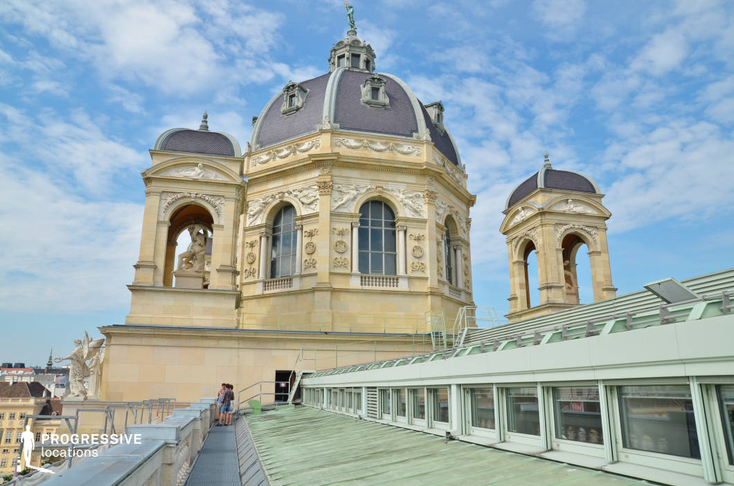 This rooftop setting features grand domed structures adorned with intricate sculptural reliefs, arched windows, and classical statues, exuding a sense of historical prestige. The elegant stonework, rich ornamentation, and dark mansard-style roofing contrast beautifully with the lighter sandstone façade. A metal walkway and modern glass skylights provide access to the structure, blending historical architecture with contemporary functionality. The elevated vantage point offers sweeping views of the surrounding cityscape, enhancing the location’s cinematic potential. This site is ideal for period dramas, historical thrillers, or espionage films, providing a dramatic and visually striking setting for rooftop encounters, clandestine meetings, or regal perspectives.