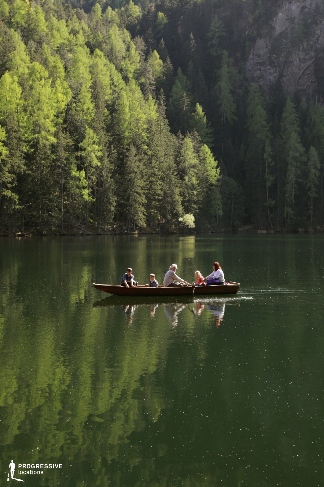 This peaceful forest lake is encircled by densely packed pine trees, whose vibrant green tones reflect clearly on the glassy surface of the water. The lake is framed by steep, wooded slopes and distant rock formations, creating a sheltered, immersive atmosphere. The water’s dark emerald hue and minimal surface disturbance enhance the setting’s sense of calm and introspection. This location is ideal for drama, nature-themed films, or emotionally resonant scenes requiring quiet natural beauty and strong vertical visual elements, especially where isolation and connection to the environment are key thematic components.